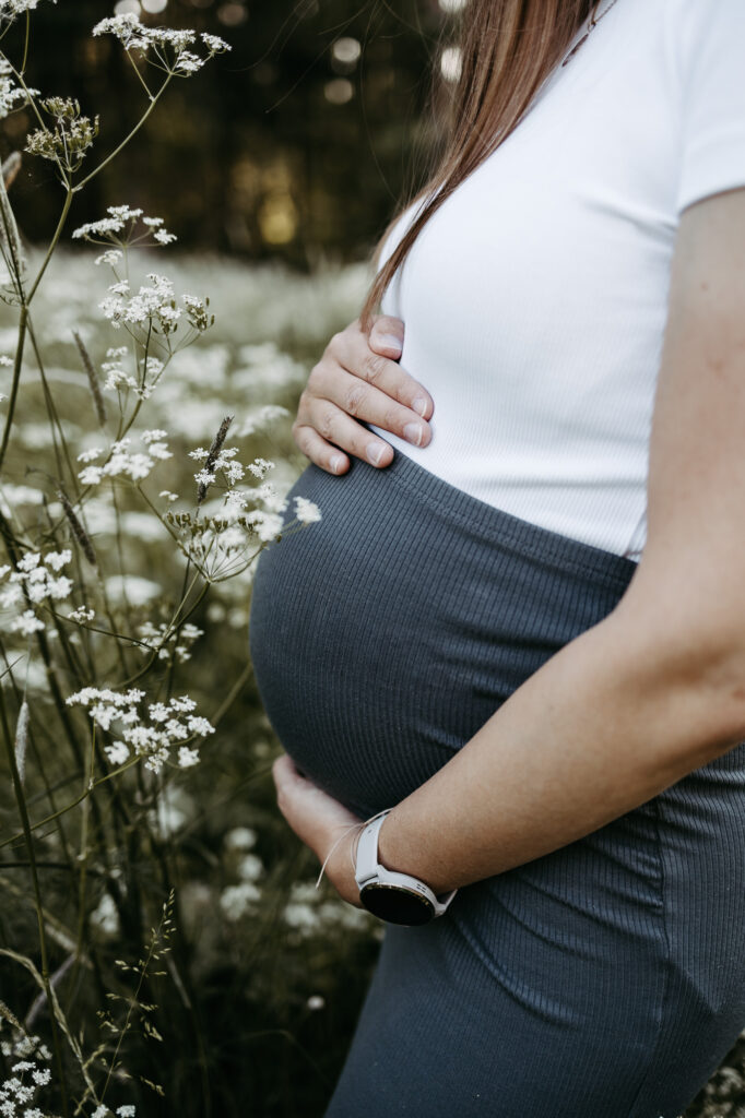 Detail: Hand auf dem nackten Babybauch, Wiese im Hintergrund