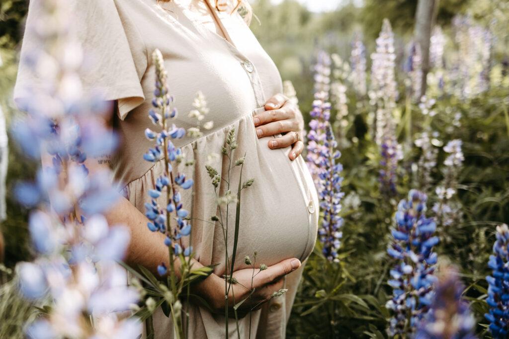 Detail: Hand am Bauch, Lupinenblüte nah im Vordergrund, warmes Licht