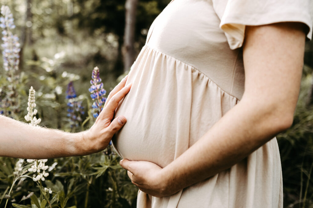 Detail: Hand am Bauch, Lupine unscharf im Vordergrund
