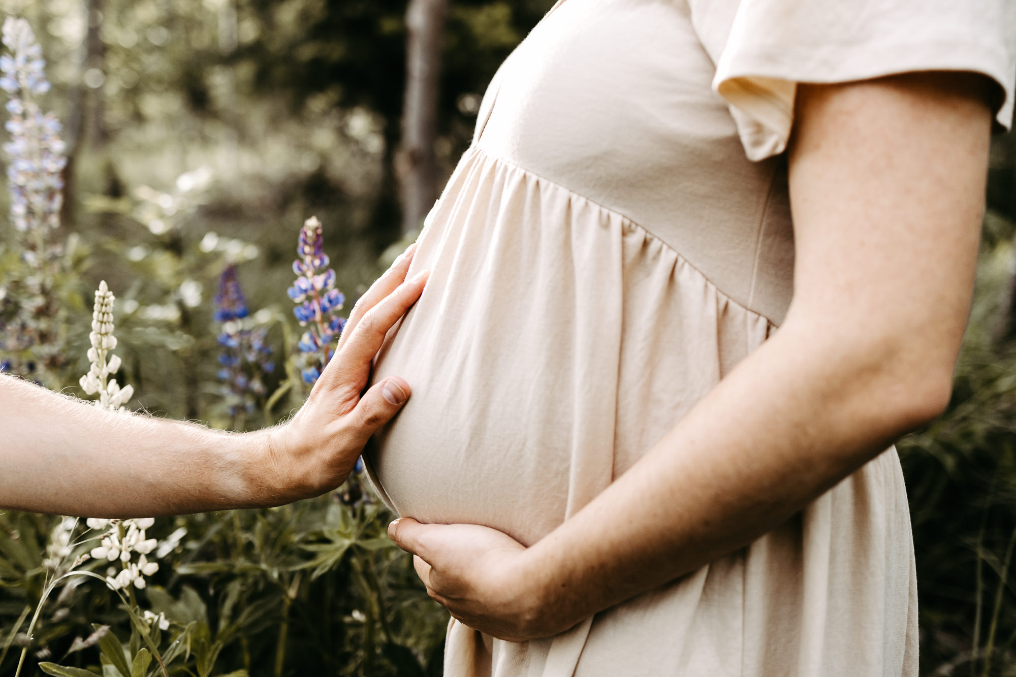 Detail: Hand am Bauch, Lupine unscharf im Vordergrund