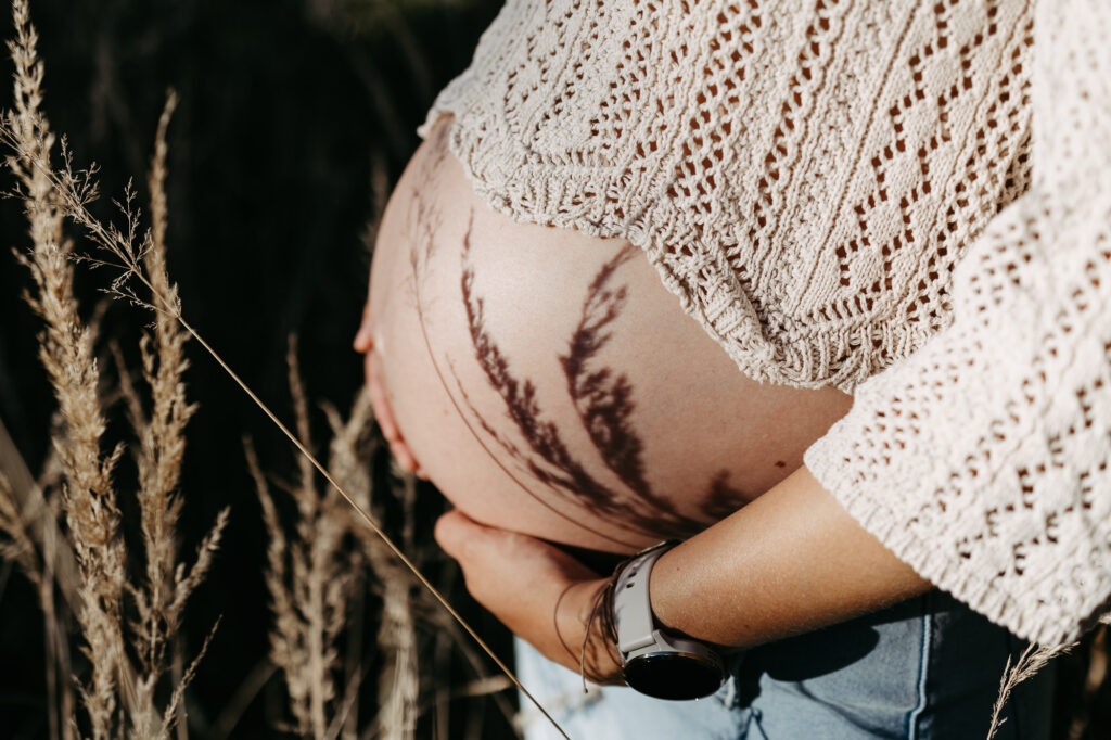 Detail: Schattenmuster von Gräsern zeichnet sich auf dem nackten Babybauch ab
