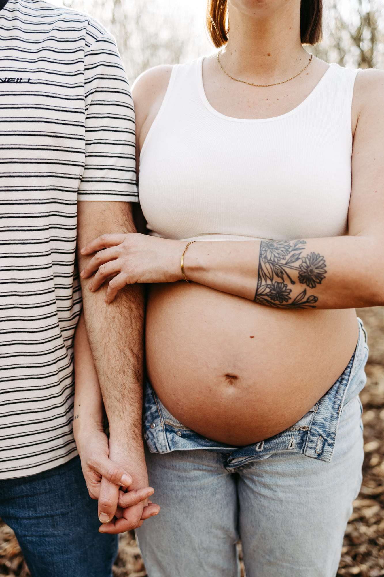Detail: Bauch und Arm der Schwangeren mit Blumentattoo, Papas Hand liegt auf ihrem Arm