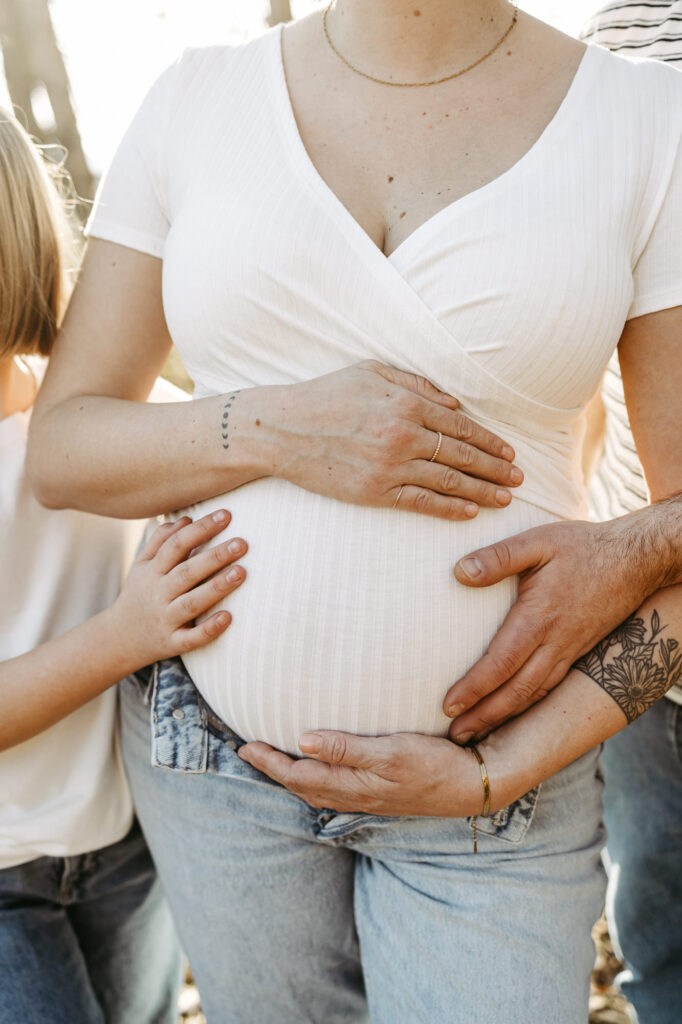 Detail: Hände von Mama, Papa und Tochter liegen gemeinsam auf dem nackten Babybauch