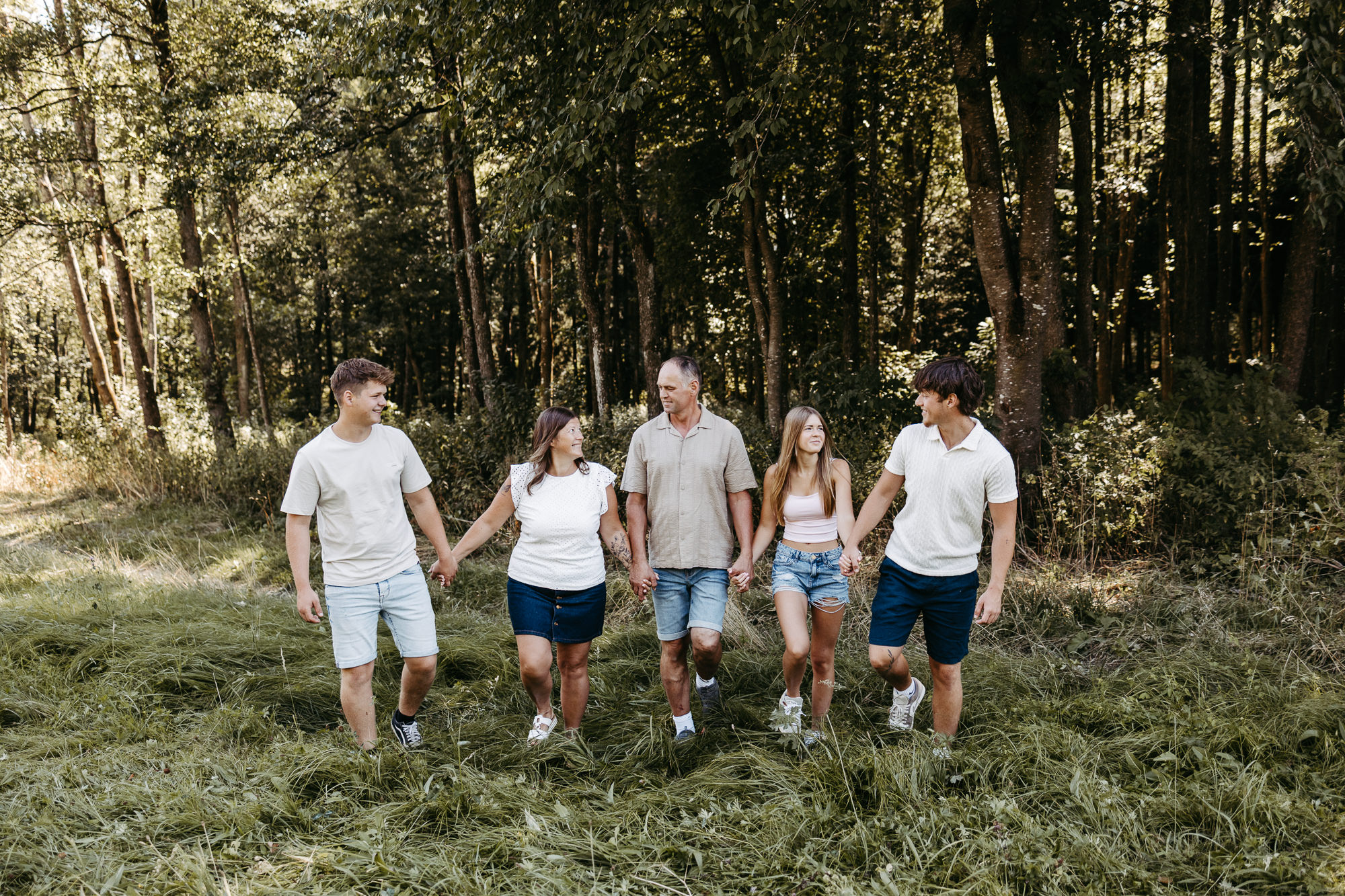 Familie geht händchenhaltend über eine Wiese und lächelt sich an