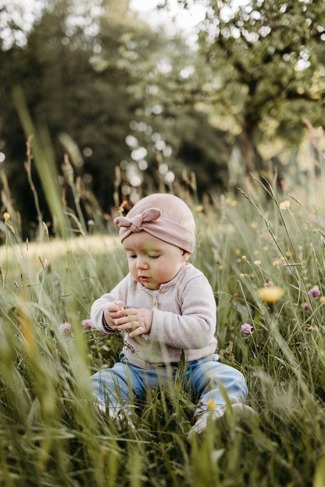 Baby sitzt allein im hohen Gras und spielt mit Wiesenblumen