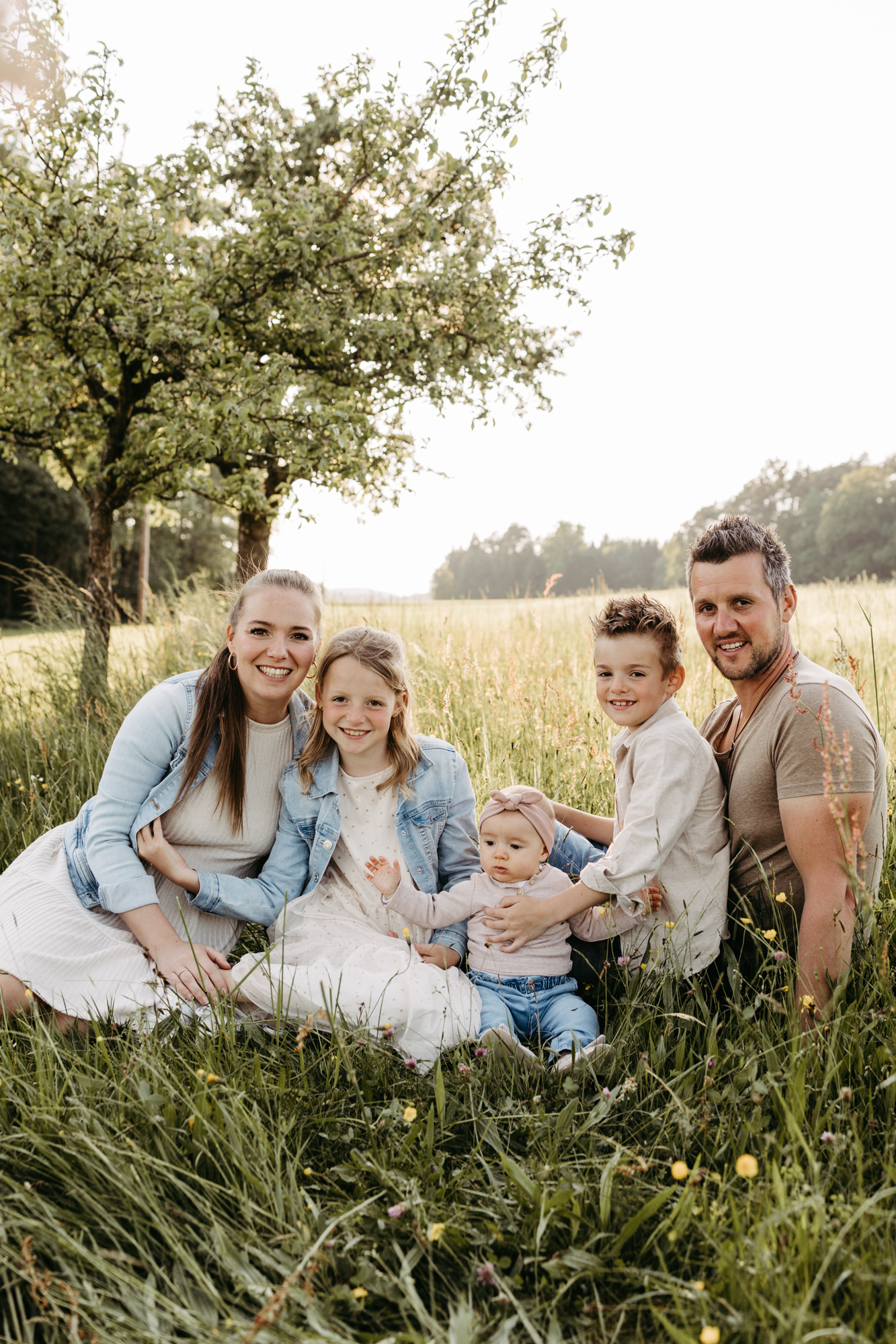Familie sitzt gemeinsam im Gras unter einem Apfelbaum und lächelt in die Kamera