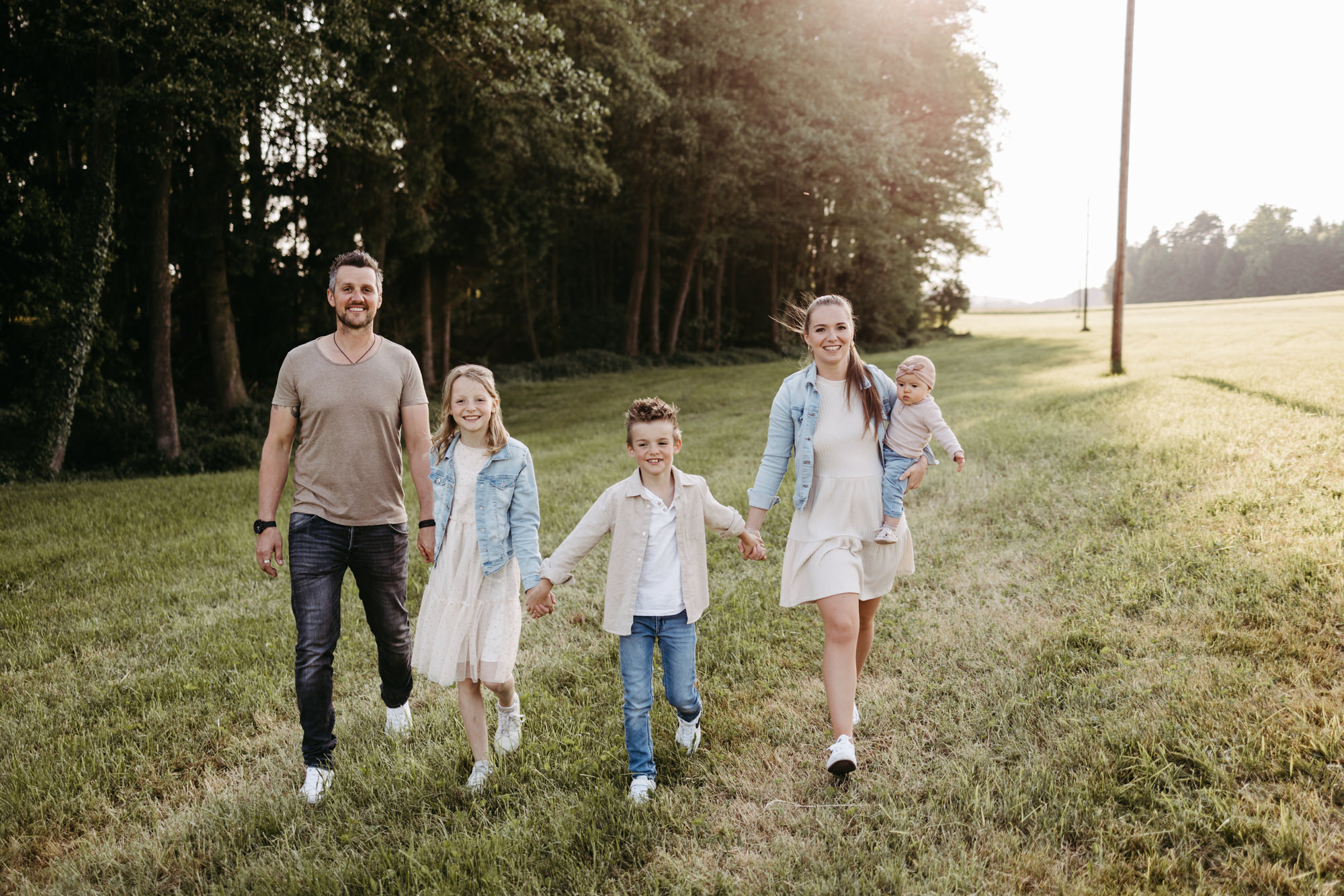 Familie geht Hand in Hand über eine Wiese und lächelt in die Kamera