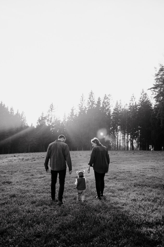 Familie geht Hand in Hand über eine Wiese, Rückenansicht, Schwarz-Weiß