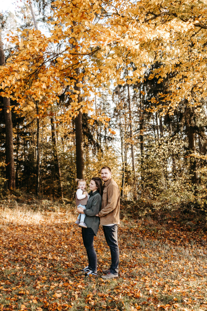 Familie steht zusammen unter einem herbstlich gefärbten Baum im Wald