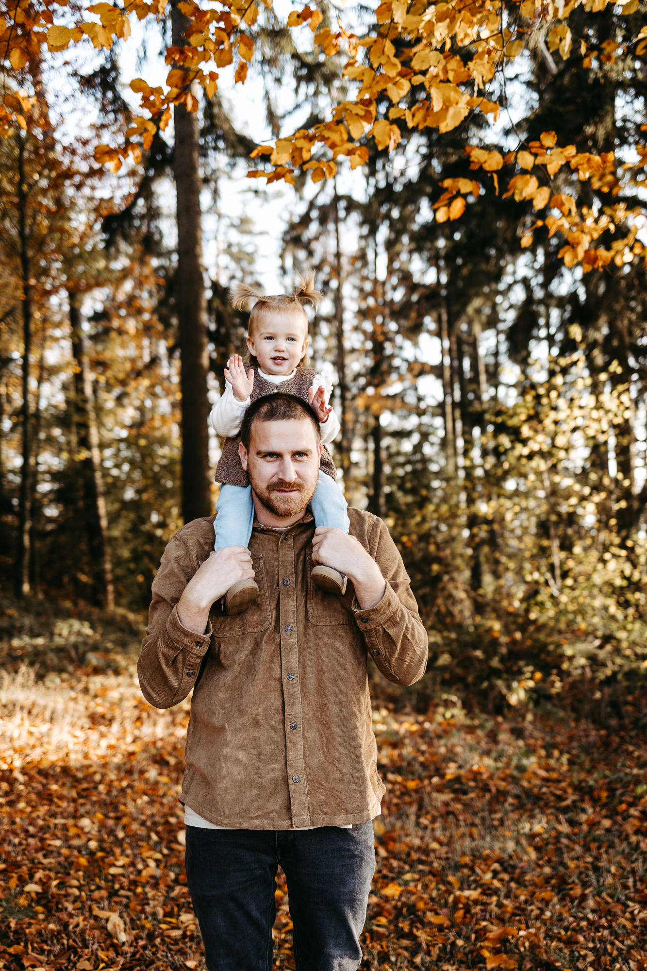 Vater trägt seine Tochter auf den Schultern, beide lächeln in die Kamera, Herbstwald
