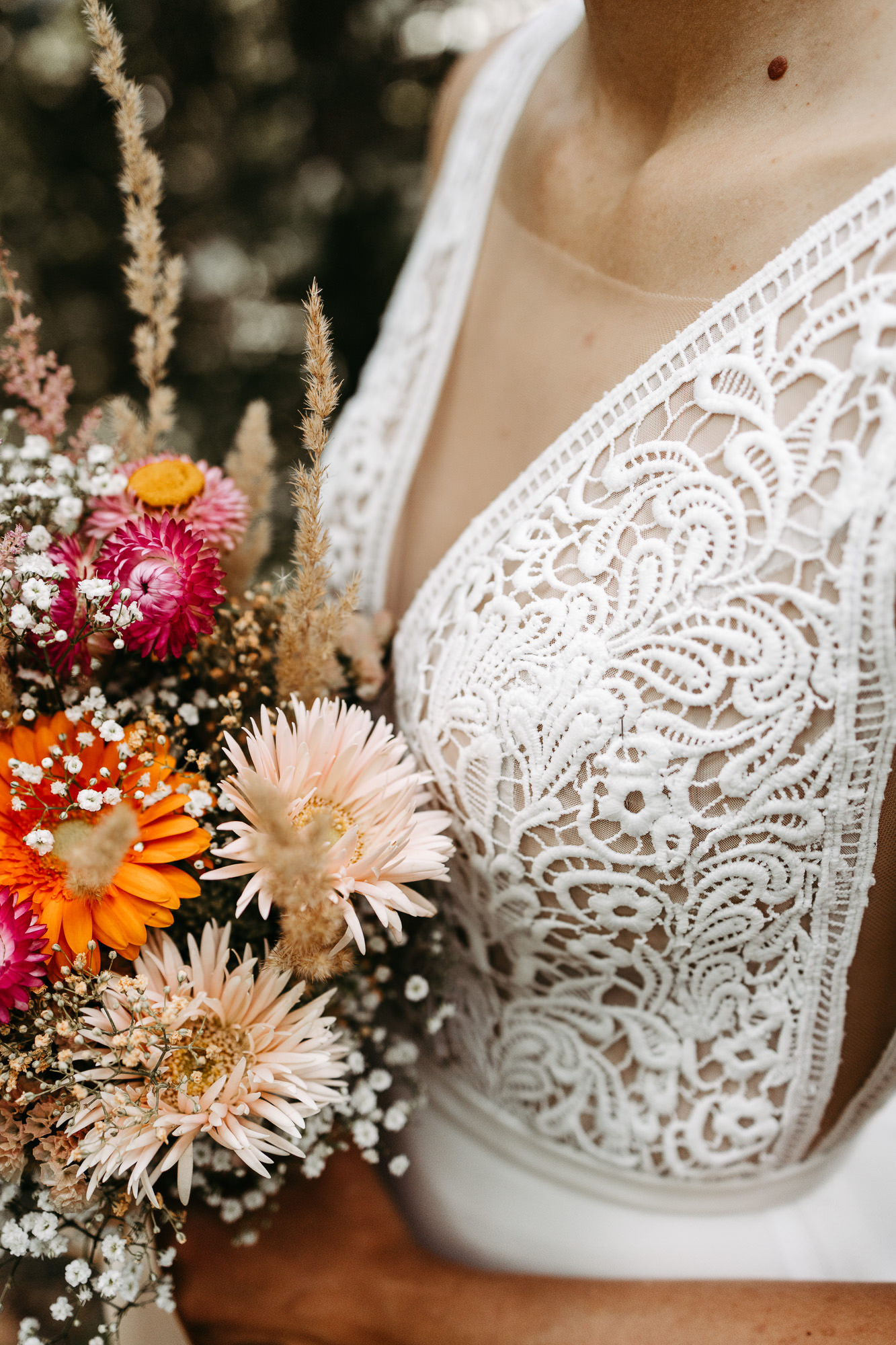 Nahaufnahme des bunten Trockenblumenstraußes am Spitzenkleid der Braut