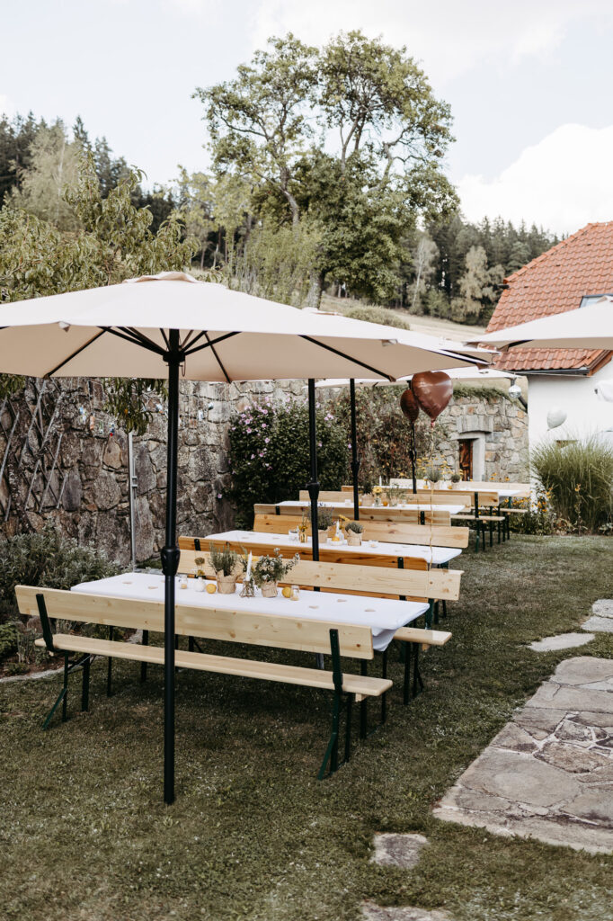 Festlich gedeckte Bierbank-Tische im Garten unter Sonnenschirmen, herzförmige Luftballons