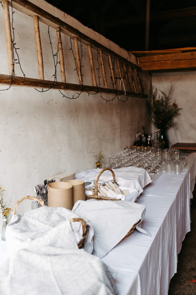 Lange Festtafel in rustikaler Scheune, Lichterkette an einer alten Holzleiter, gedeckte Gläser