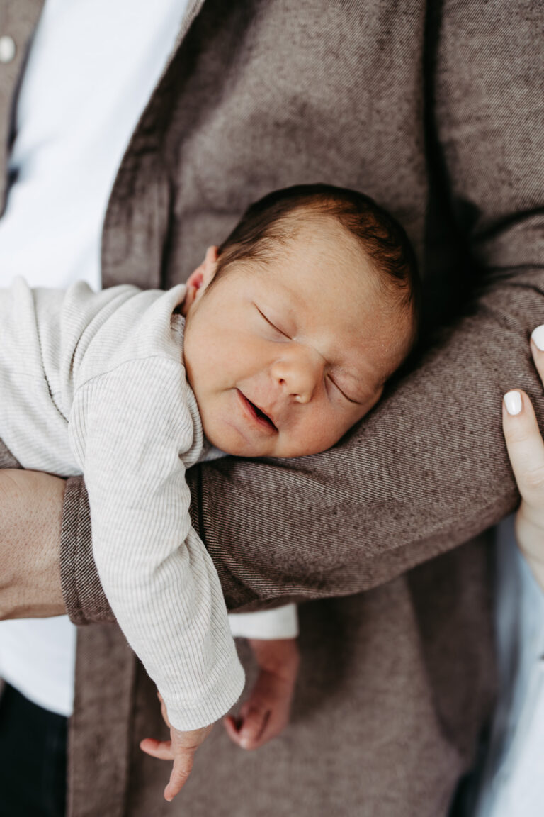 Eingewickeltes Baby liegt schlafend auf der Schulter
