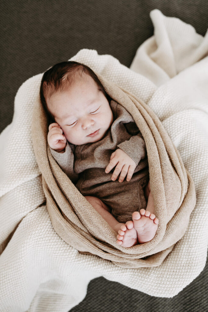 Baby liegt eingewickelt in beige-braune Strickdecke, Draufsicht, schlafend