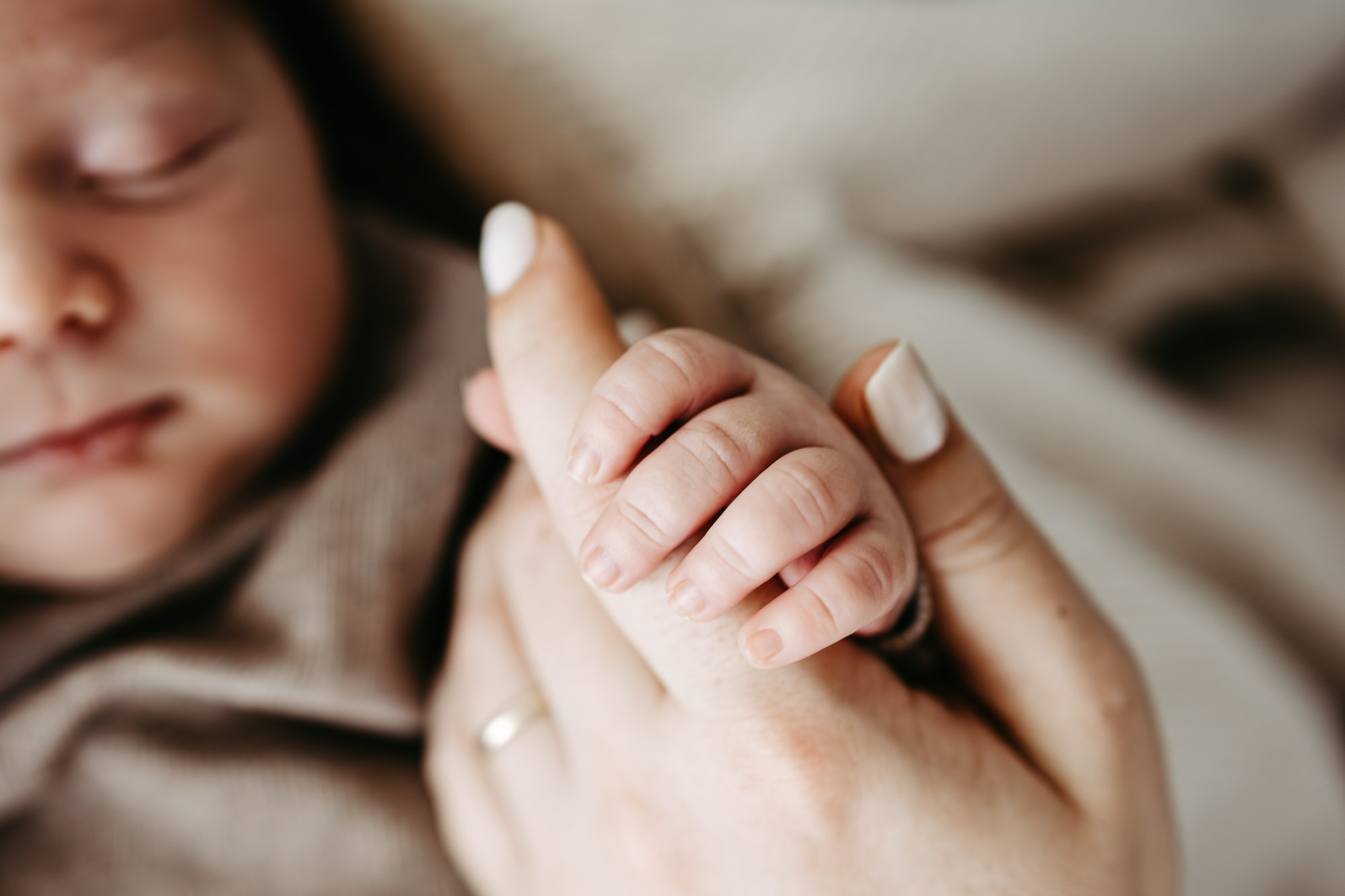 Nahaufnahme: Baby hält den Finger der Mutter, Ehering sichtbar