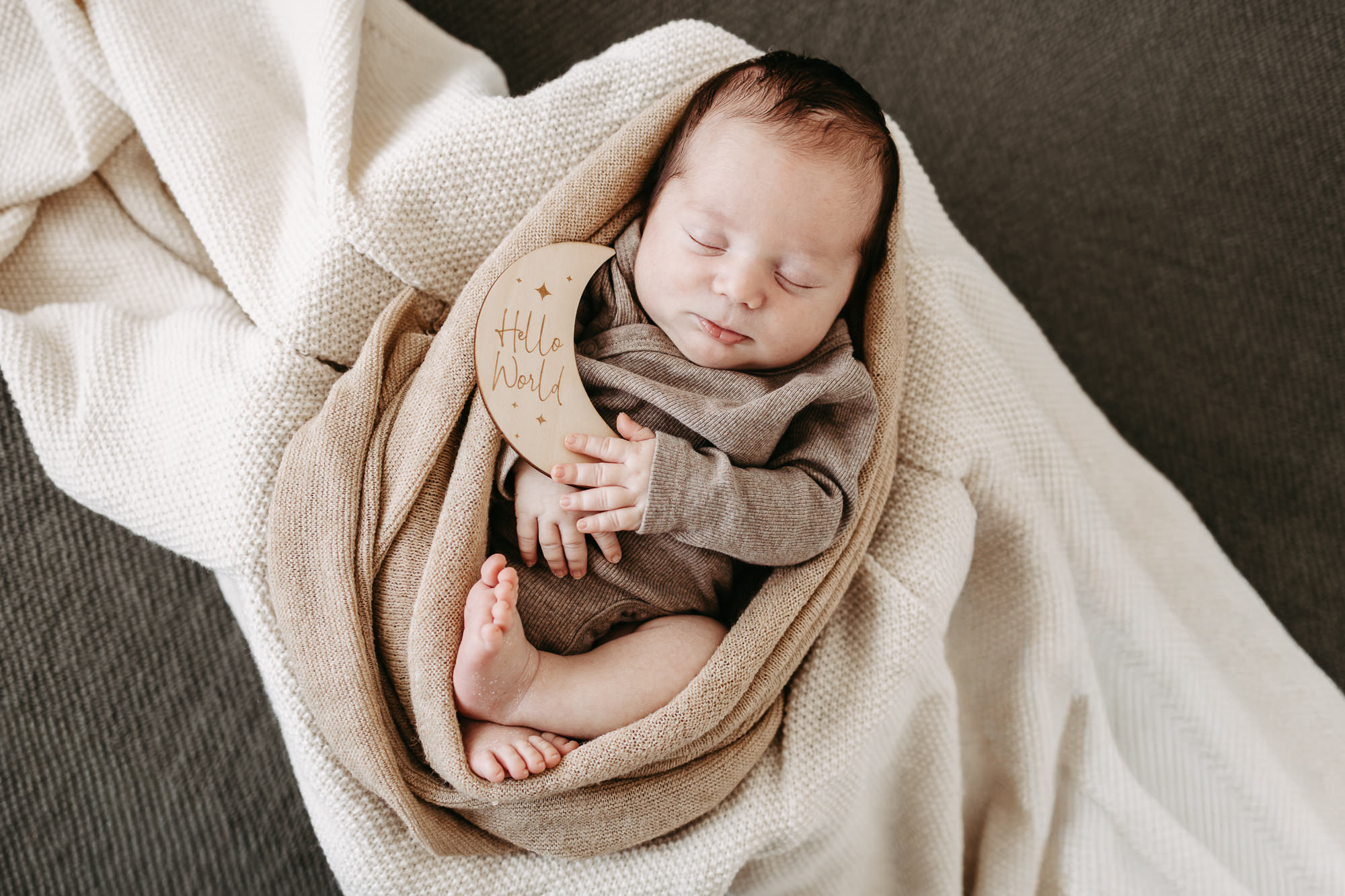 Baby liegt eingewickelt neben einem Holzschild mit der Aufschrift „Hello World", Draufsicht auf dem Sofa
