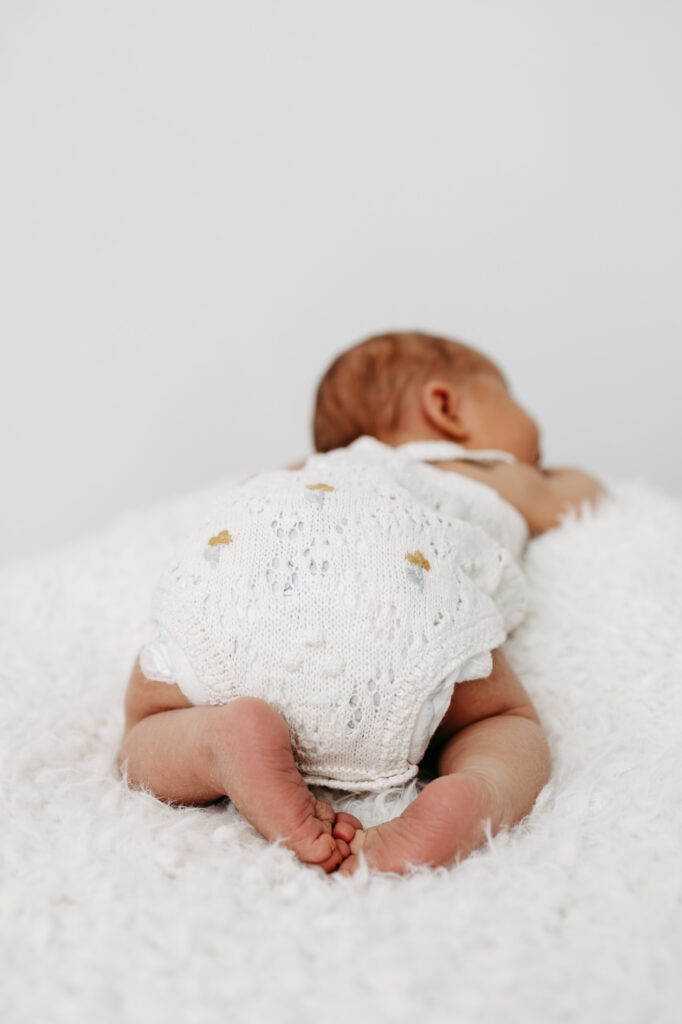 Baby liegt in Bauchlage auf einer flauschigen Decke, Rückenansicht