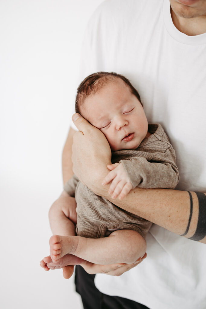 Nahaufnahme: Hände der Eltern halten Füßchen und Hand des in die Decke gewickelten Babys, Schwarz-Weiß