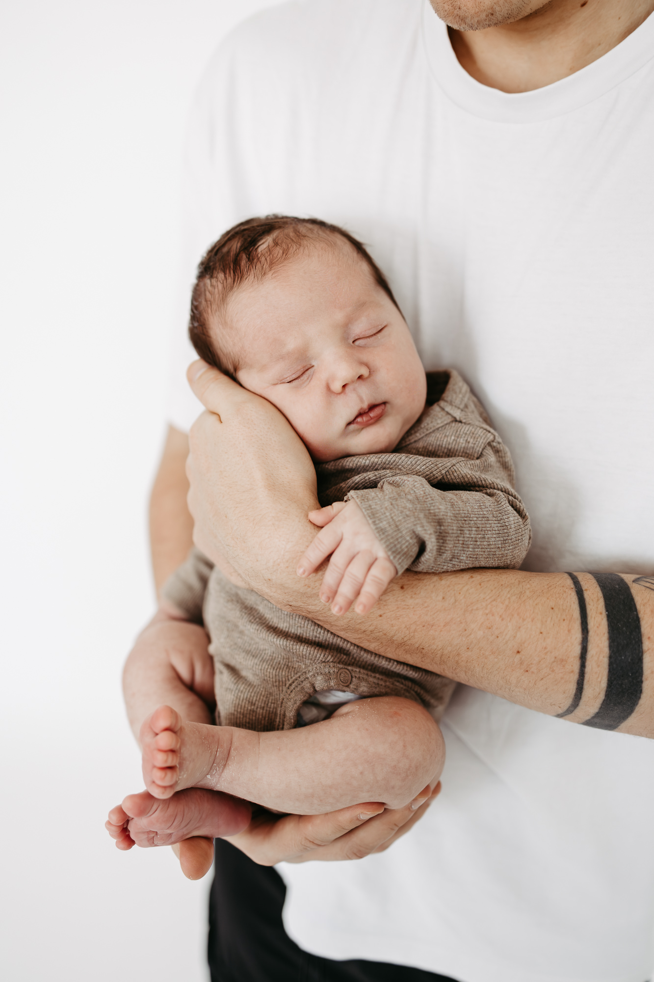 Nahaufnahme des schlafenden Babygesichts auf dem Arm des Vaters, Tattoo sichtbar