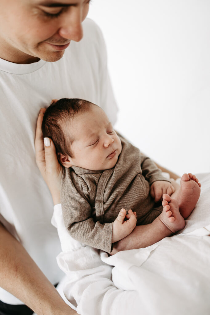 Baby schläft, Kopf wird sanft von einer Hand gehalten, an der Brust des Vaters