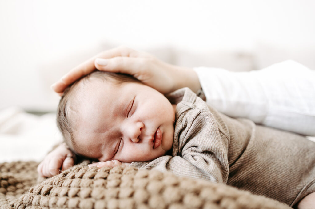 Baby schläft auf dem Kissen, Mutters Hand ruht sanft auf seinem Kopf