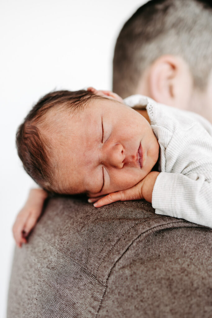 Baby schläft auf der Schulter, im Hintergrund unscharf eine zweite Person
