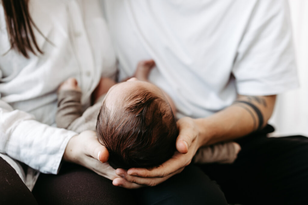 Nahaufnahme: Baby liegt auf Vaters Arm, Kopf wird gehalten, blickt zur Kamera