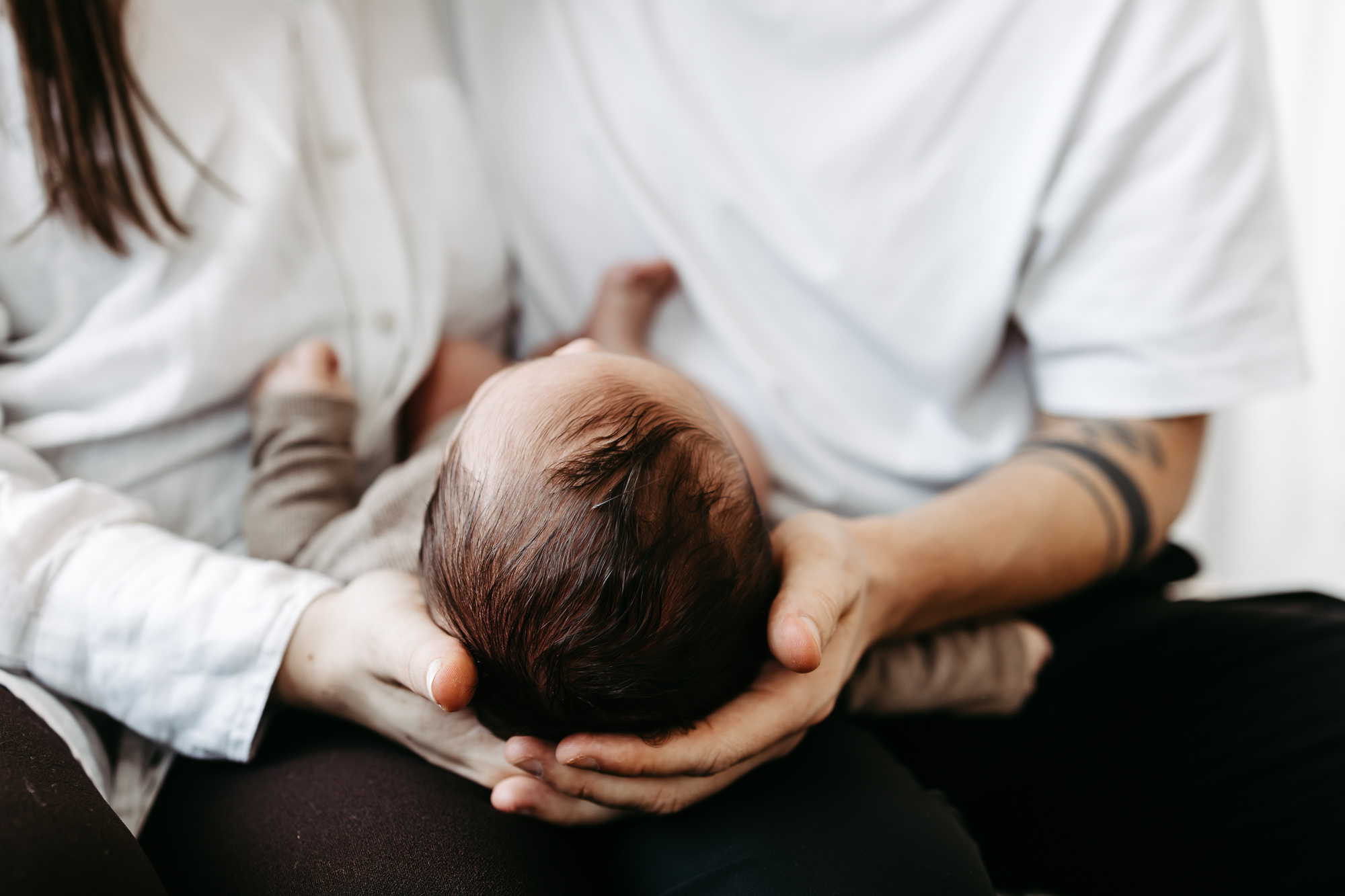 Nahaufnahme: Baby liegt auf Vaters Arm, Kopf wird gehalten, blickt zur Kamera