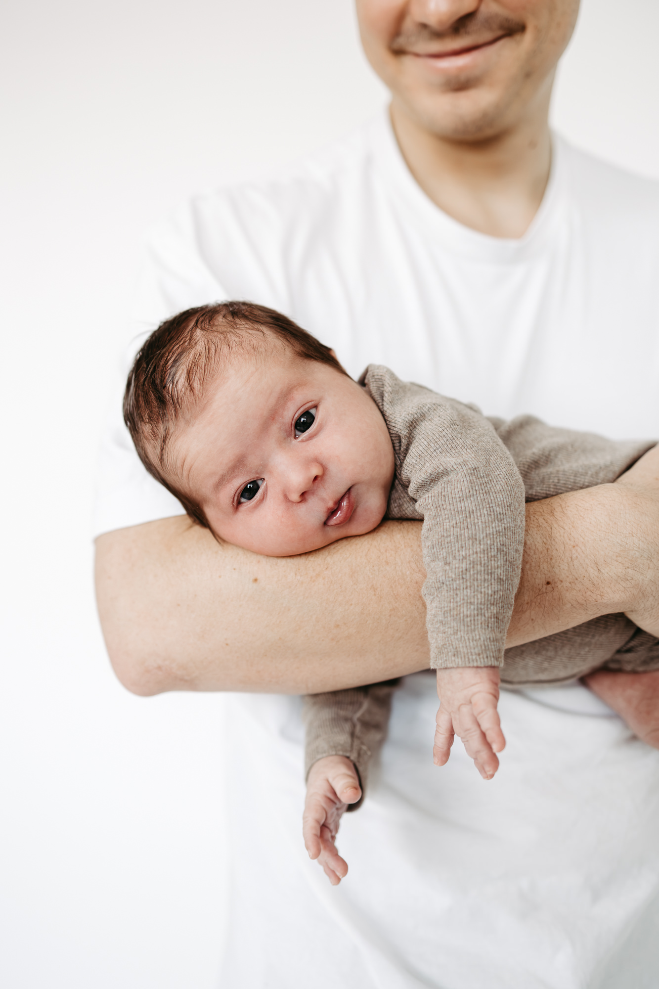 Baby liegt auf Vaters Arm, blickt zur Kamera, weißer Hintergrund