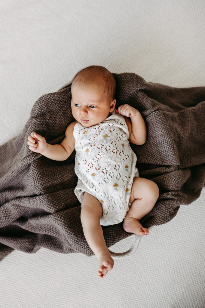 Baby liegt eingekuschelt in einer braunen Wolldecke und blickt zur Seite