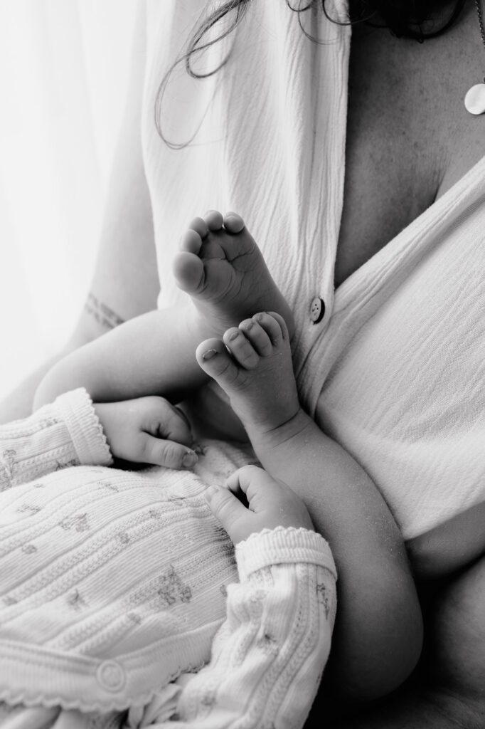 Schwarz-weiß-Detailaufnahme der Babyfüßchen an der Brust der Mutter