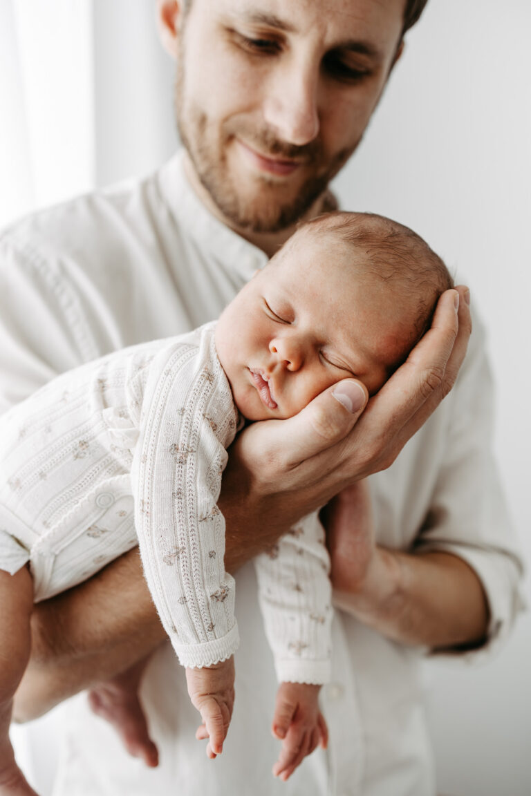Detailaufnahme: das schlafende Babygesicht ruht in der Hand des Vaters