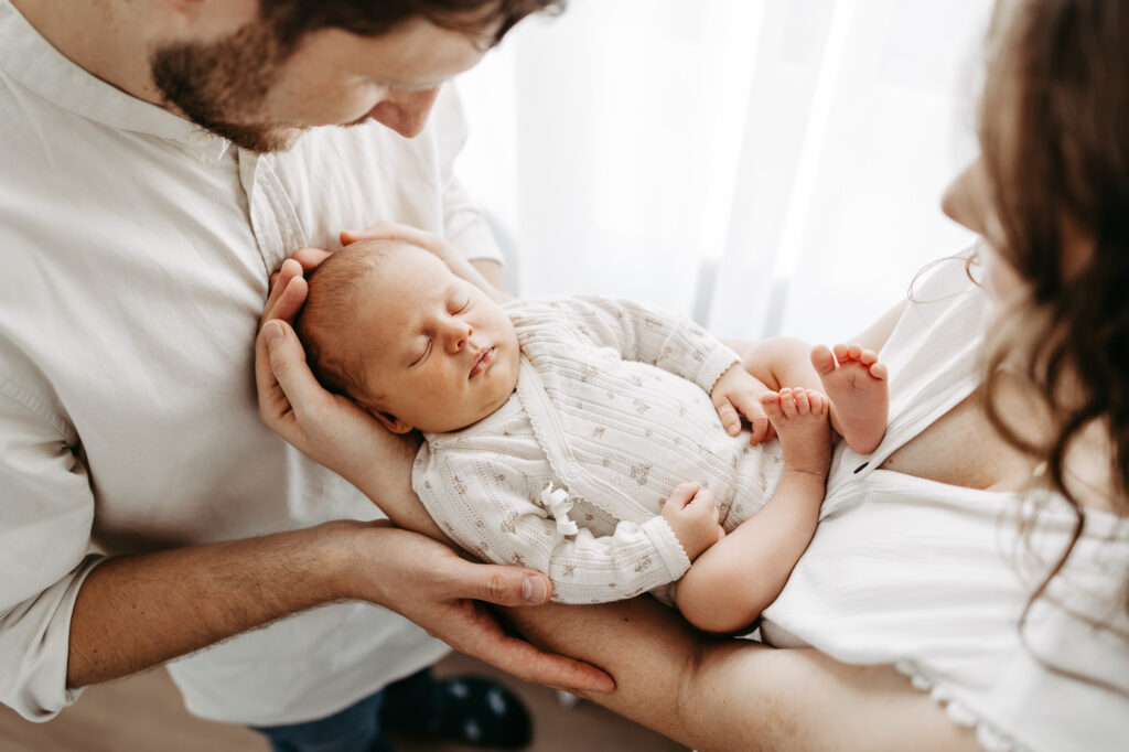 Detailaufnahme am Fenster: die Hände der Eltern halten sanft den Kopf des Babys
