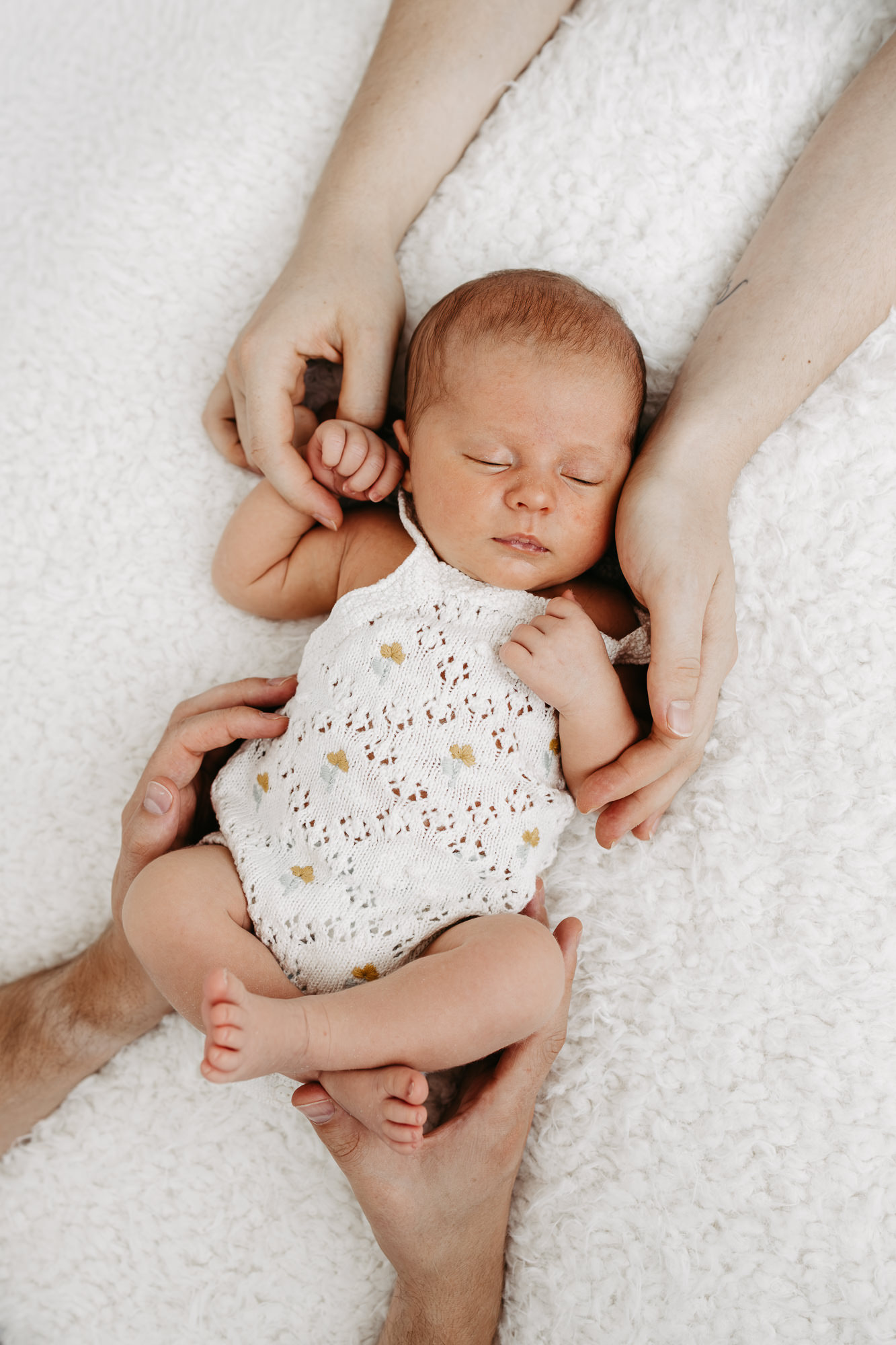 Detailaufnahme von oben: die Hände der Eltern halten Händchen und Füßchen des liegenden Babys