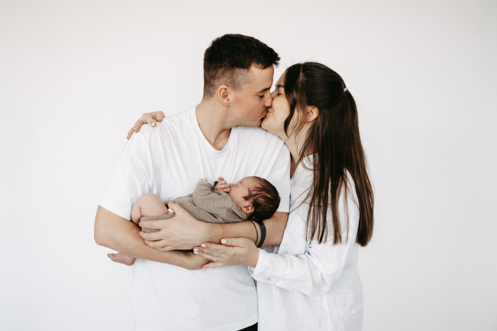 Eltern küssen sich, während sie das schlafende Baby gemeinsam halten