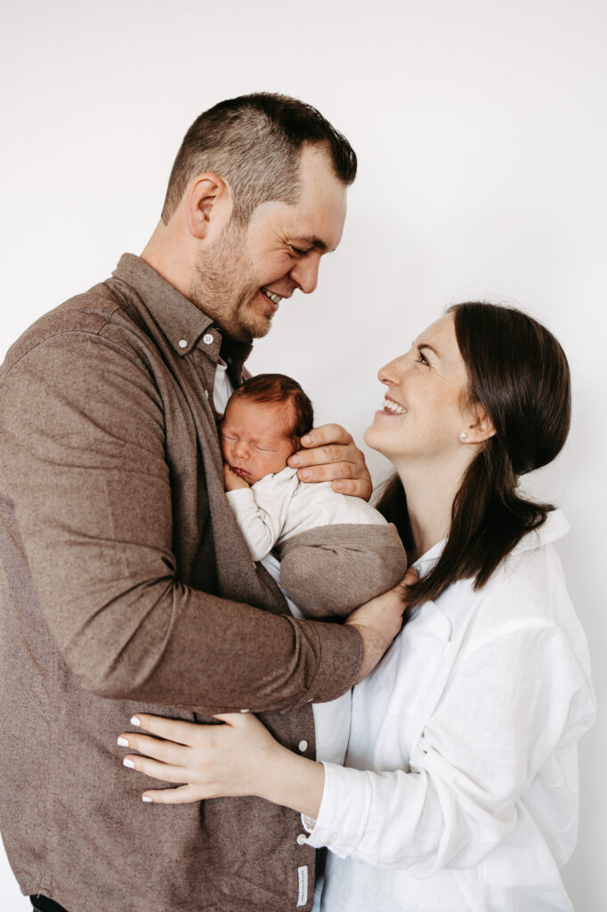 Eltern lachen sich über ihrem Baby an, der Vater hält es auf dem Arm