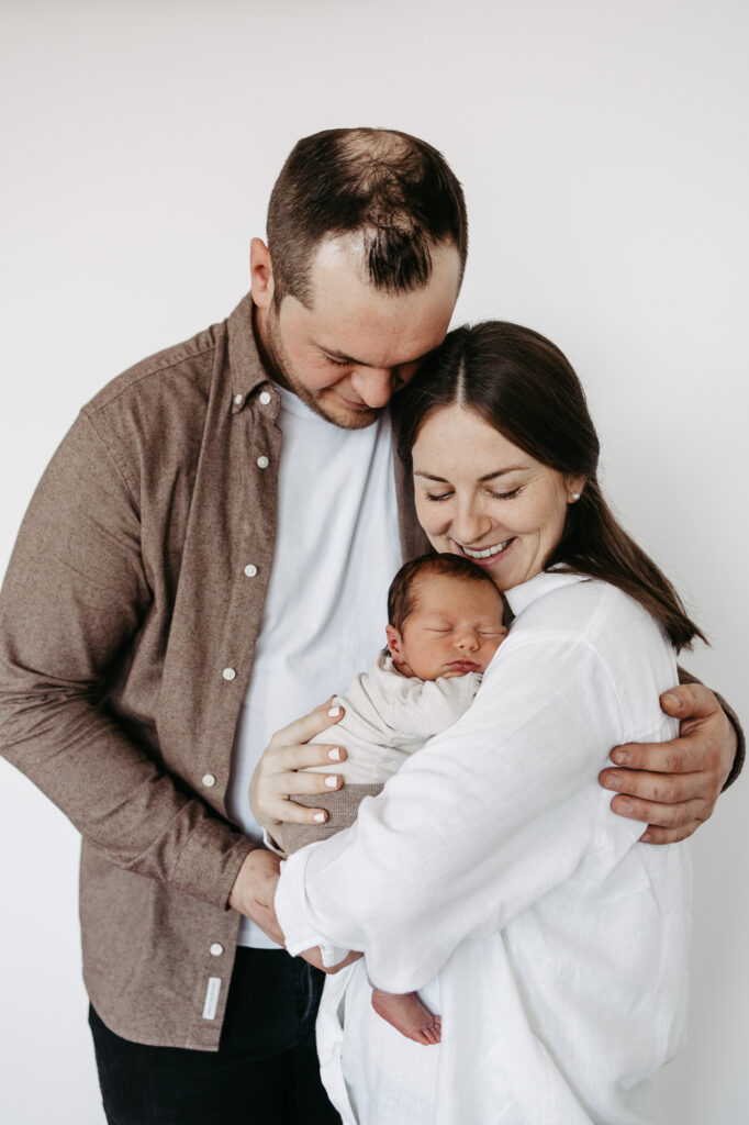 Eltern halten gemeinsam lächelnd ihr Baby im Arm