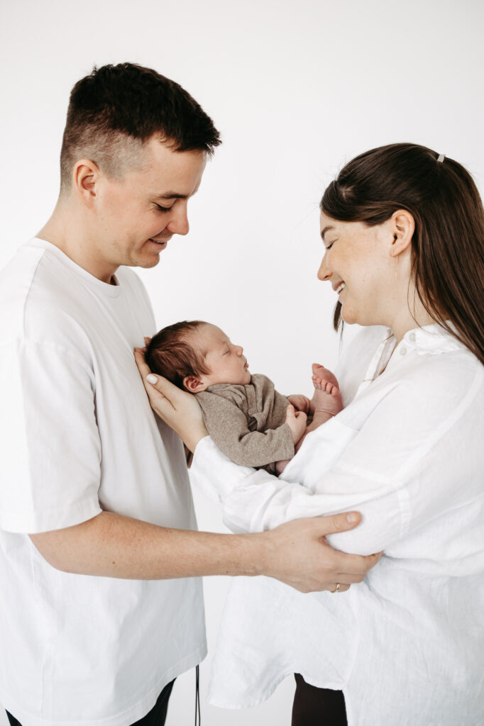 Eltern stehen Stirn an Stirn lächelnd, Baby schläft zwischen ihnen gehalten