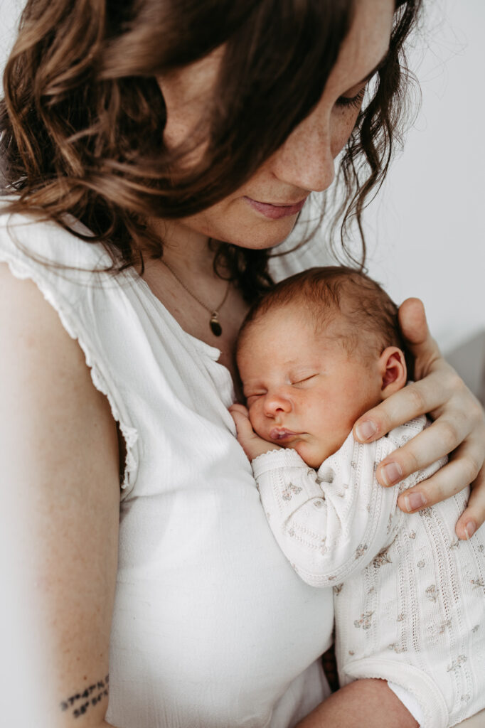 Mutter hält ihr Baby eng an die Brust, die Hand des Vaters liegt sanft am Babykopf