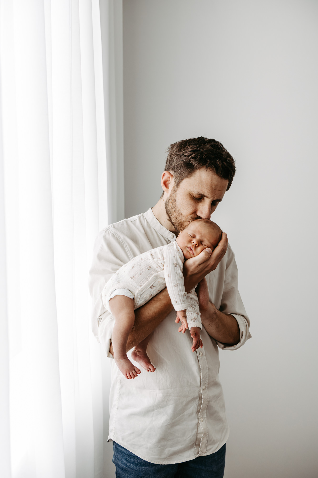 Vater steht am Fenster und küsst den Kopf seines Babys