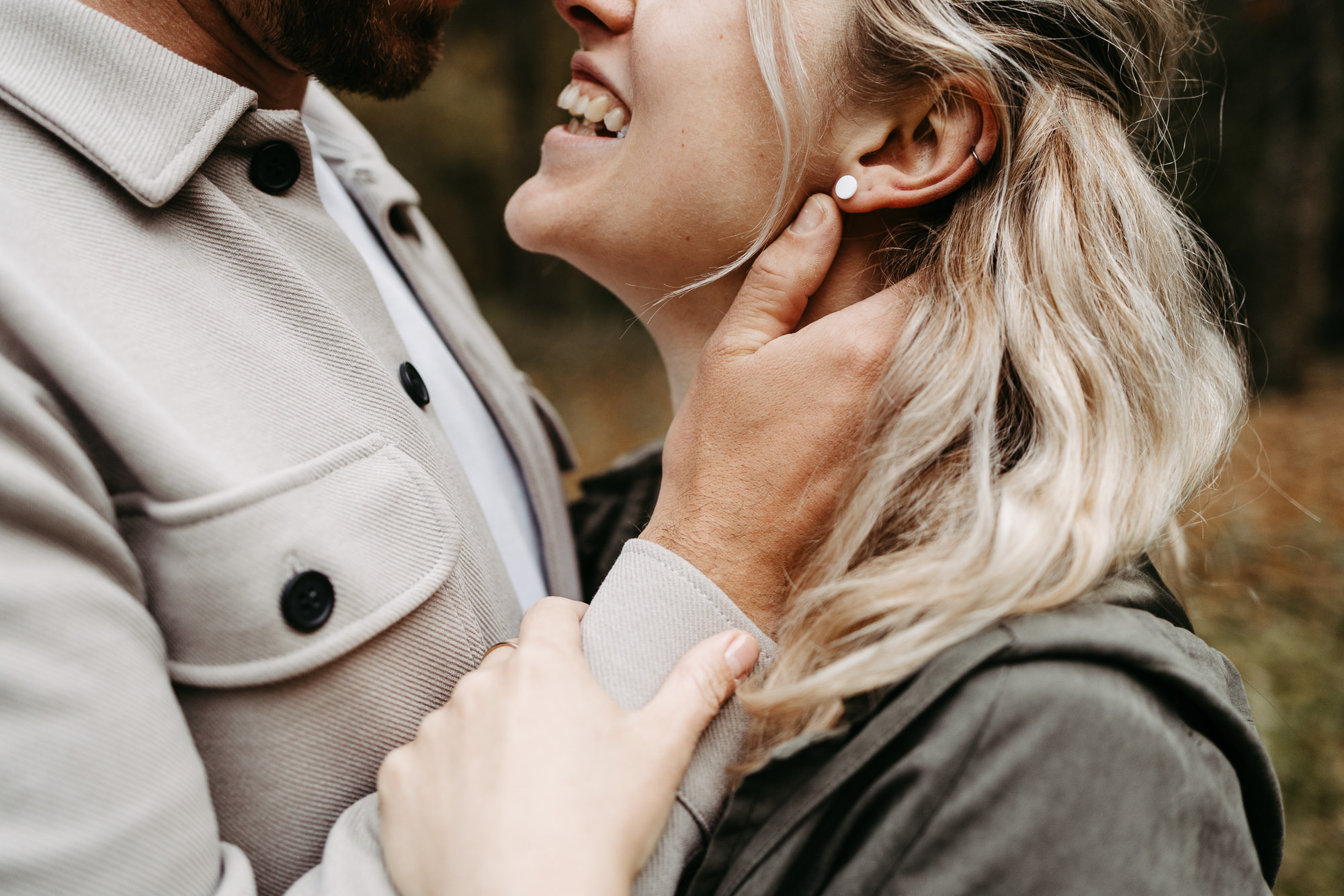 Detail: Frau lacht, Hand des Partners an ihrem Hals, Ohrring und Ohrpiercing sichtbar
