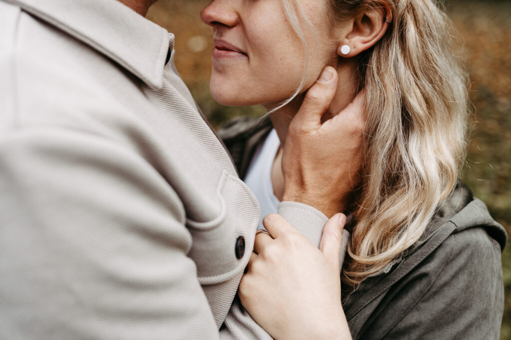 Detailaufnahme von Hals und Ohr der Frau, Ring an der Hand des Partners sichtbar