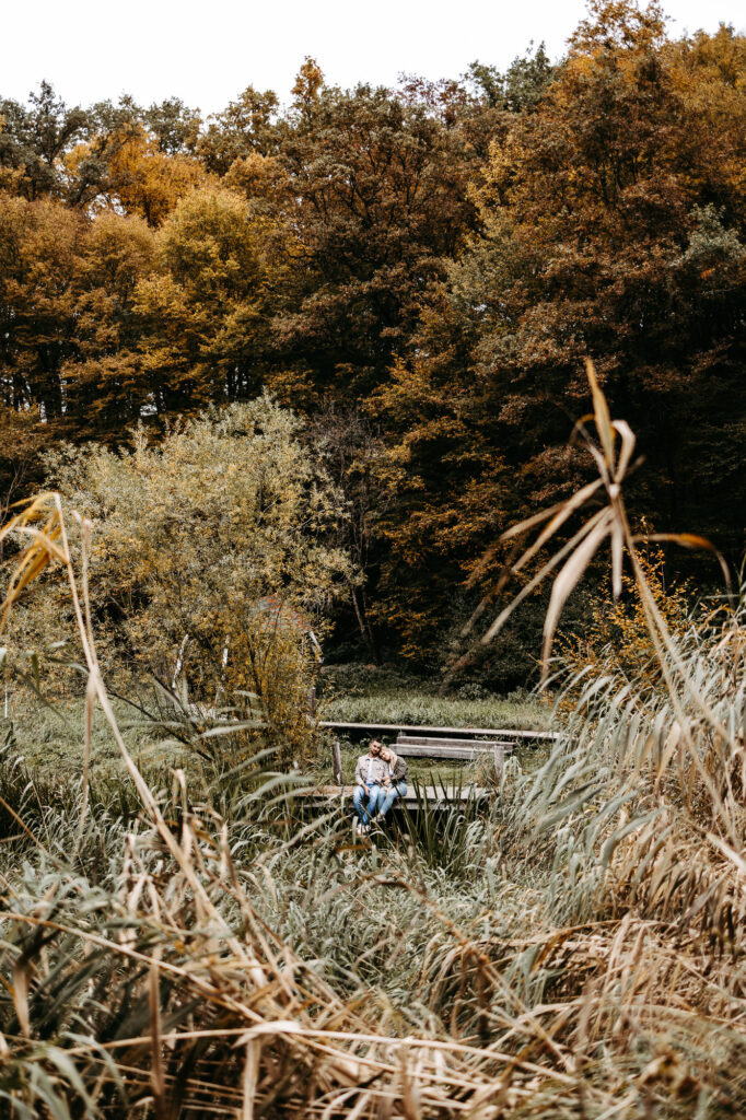 Paar sitzt eng beieinander auf einem Holzsteg am Teich, Schilf im Vordergrund