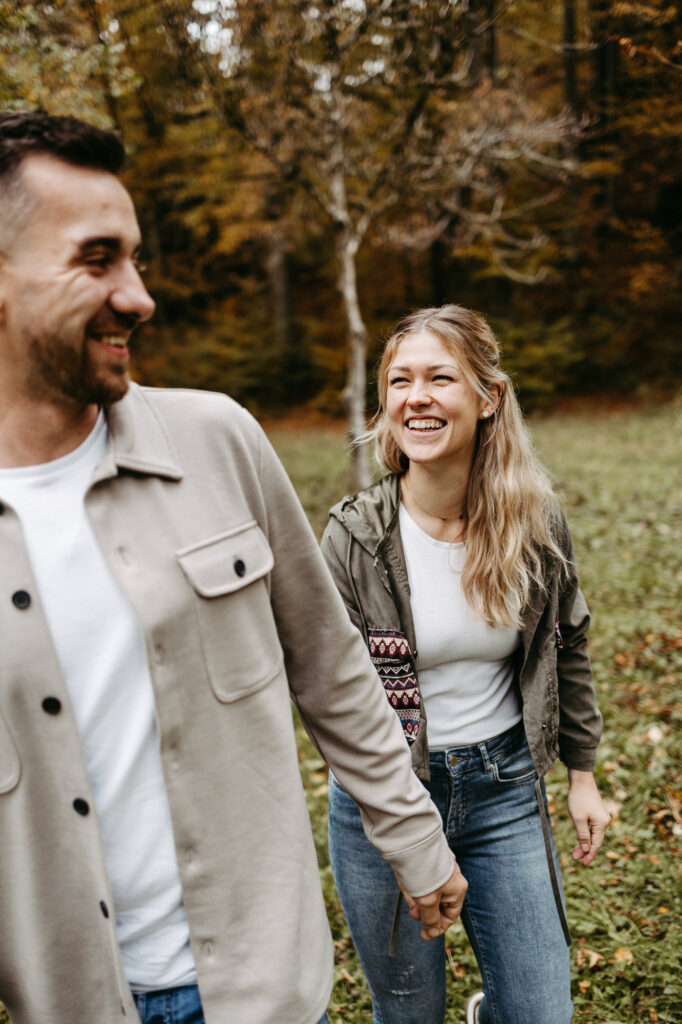 Paar geht lachend über eine Wiese am Waldrand im Herbst